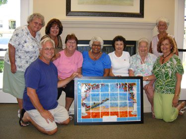 Nine people posing for a group photo holding a framed art