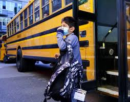 A kid wearing a mask getting off the bus